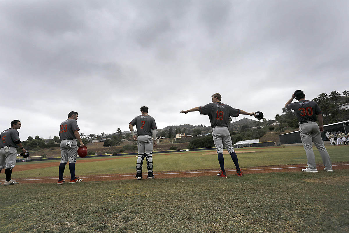 A collegiate baseball player holds his arms out to test social distancing with his teammates before starting league competition. 