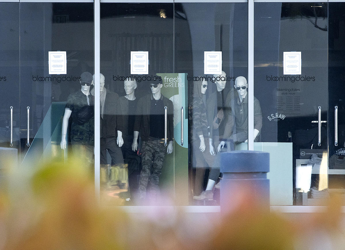 A few weeks after the start of the COVID-19 lockdown, mannequins stare out the window of a closed Bloomingdales store in San Diego with warning signs posted nearby. 
 